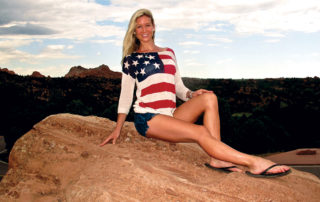 Girl sits on rock with Red, White and Blue sweater