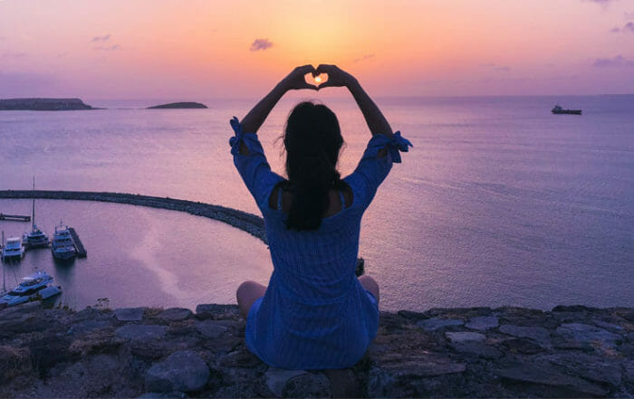 woman holding hands in shape of heart at ocean