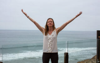 Lisa Gornall with arms up at the beach to demonstrate how to stop trying to do it all