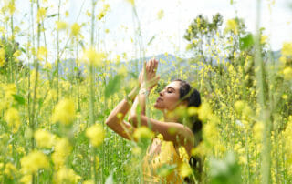 Kimberly Snyder with hands in prayer pose amidst yellow flowers