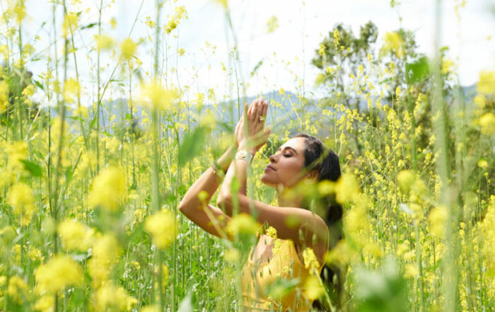 Kimberly Snyder with hands in prayer pose amidst yellow flowers