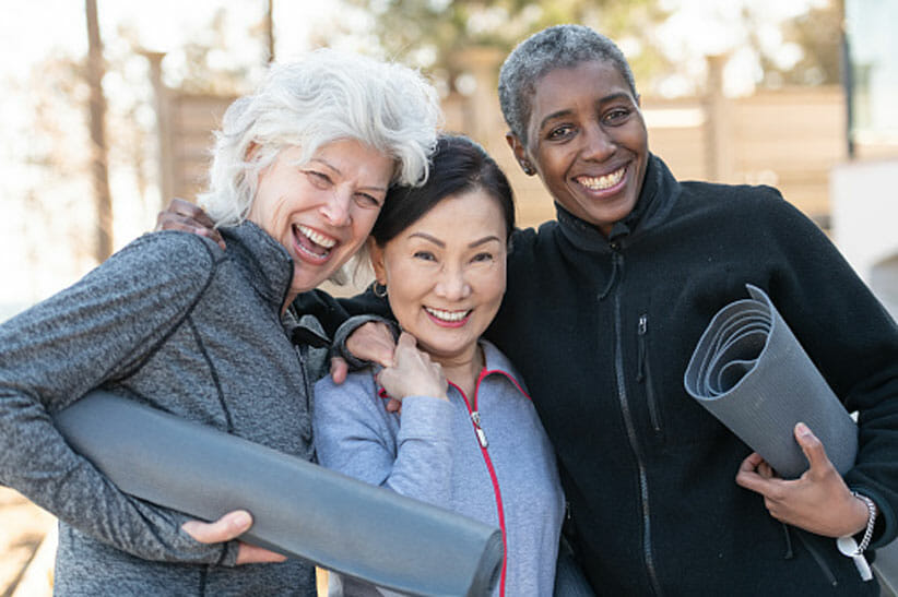three people with white hair holding yoga mats