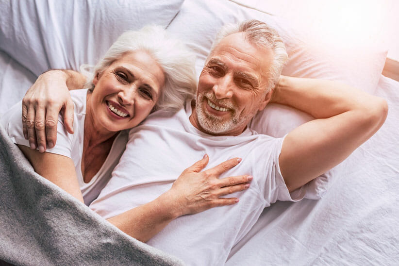 man and woman with white hair reclining smiling to camera 