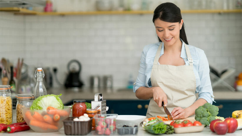 Woman with black hair in a kitchen in an uncluttered home doing food prep