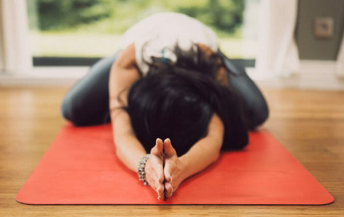 Woman in forward fold with hands in prayer on orange yoga mat demonstrating yin yoga