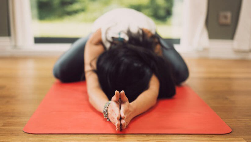 Woman in forward fold with hands in prayer on orange yoga mat demonstrating yin yoga