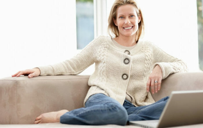 Woman smiling in white sweater on couch sitting in an uncluttered home