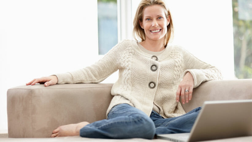 Woman smiling in white sweater on couch sitting in an uncluttered home