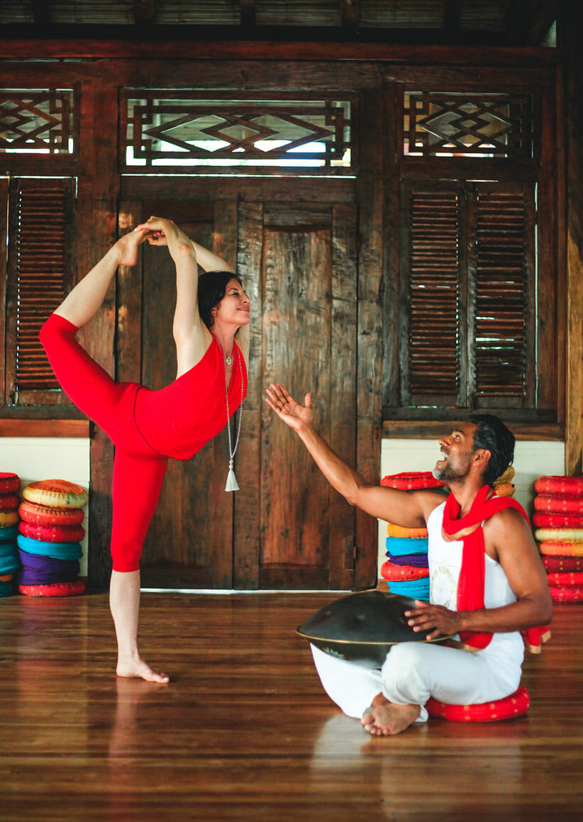 woman in red in yoga pose and man playing hang drum