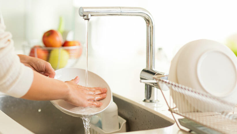 person hand-washing dishes in the sink