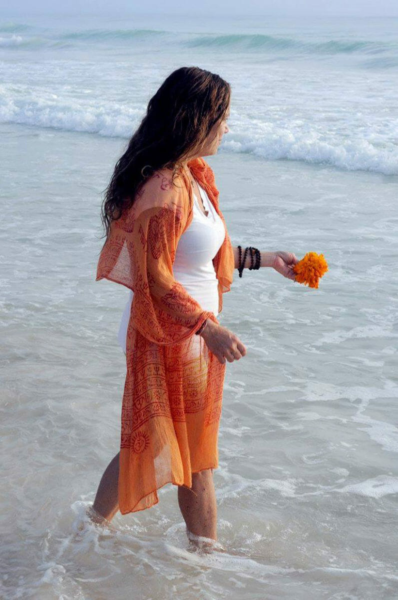 woman in orange offering flowers to ocean to demonstrate how to make gratitude a spiritual practice