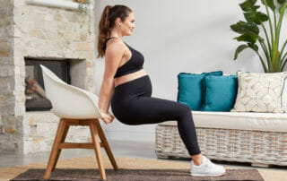 Emily Skye Demonstrating how to debunk pregnancy fitness myths but doing dips on a chair in living room