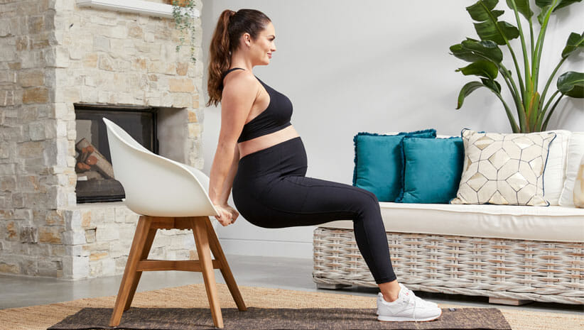 Emily Skye Demonstrating how to debunk pregnancy fitness myths but doing dips on a chair in living room 