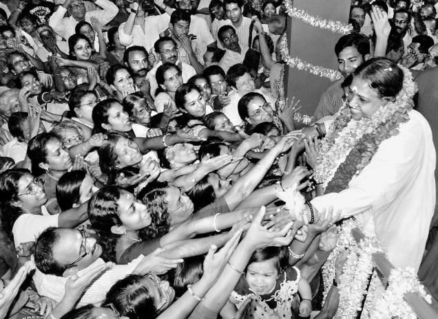 Black and white photo of a crowd of people with their hands reaching to Amma, the Hugging Saint