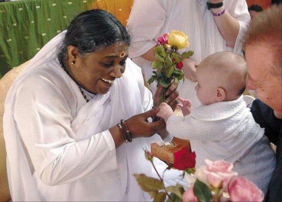 Small baby held by an adult offering flowers to Amma