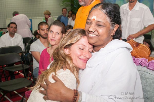 Smiling woman being hugged by Amma, the Hugging Saint, with people watching