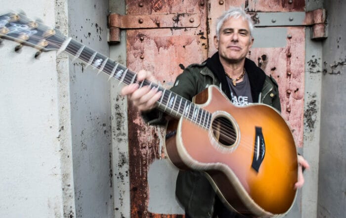 Sacred musical artist Jai Uttal holding a guitar angled toward the viewer