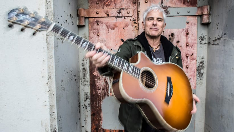 Sacred musical artist Jai Uttal holding a guitar angled toward the viewer