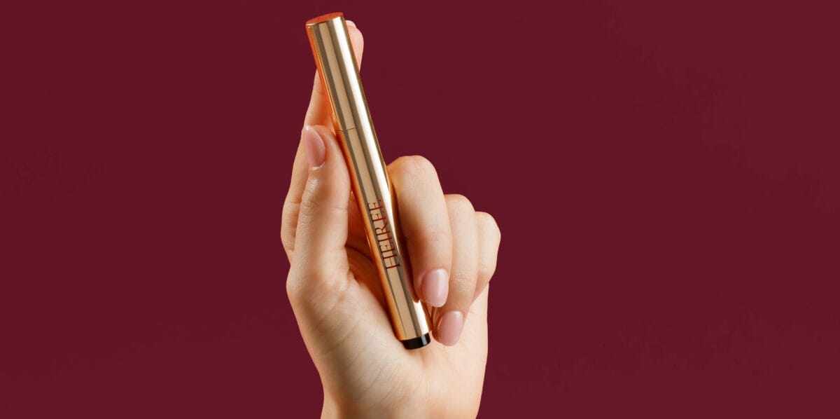 well-manicured hand holding HEIREE Cuticle pen with a red background