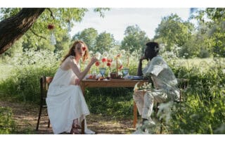 Two people sitting at a picnic table in the midst of a field of flowers for summer picnics