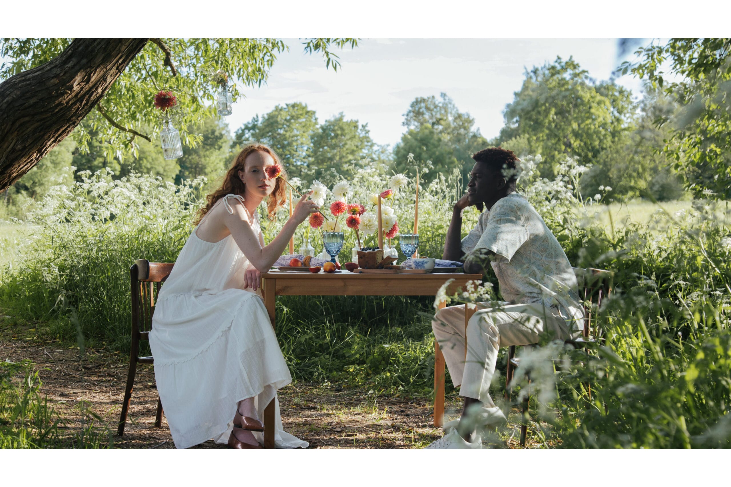 Two people sitting at a picnic table in the midst of a field of flowers for summer picnics