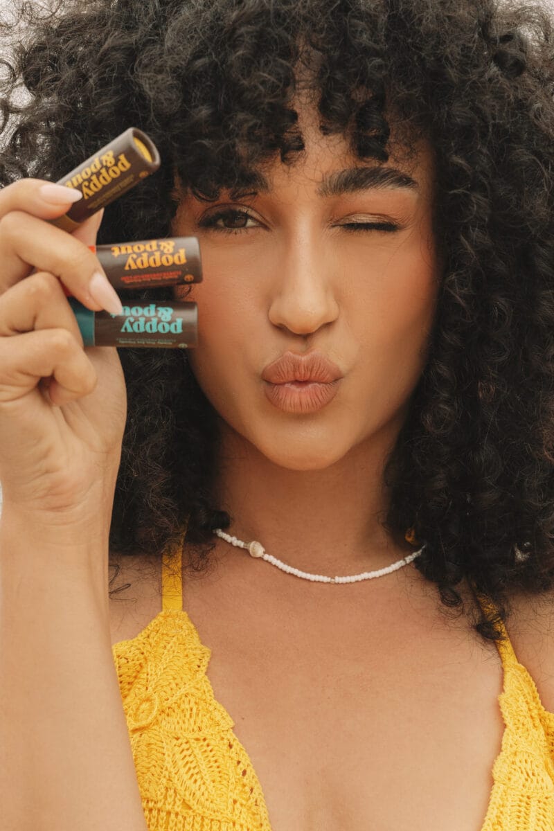 woman with yellow shirt holding up three lip balms