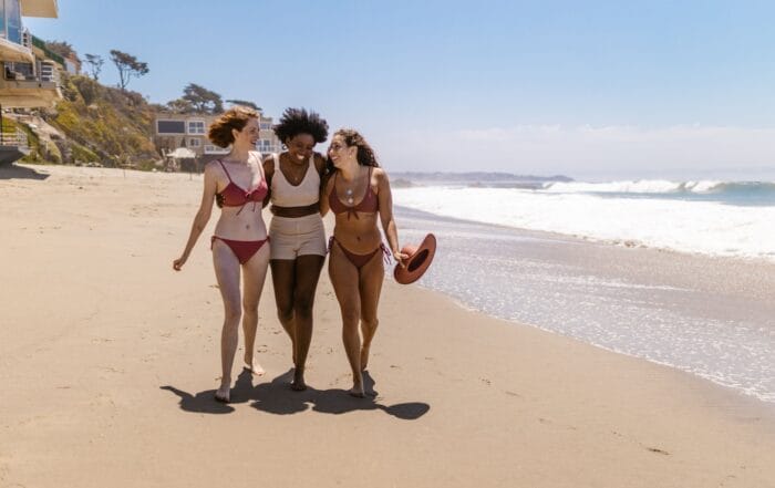 Three women in bikinis walking down the beach